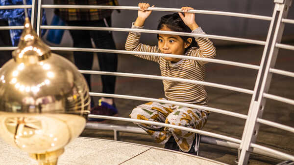 A young girl watches the Foucault pendulum knock down pins at the Academy