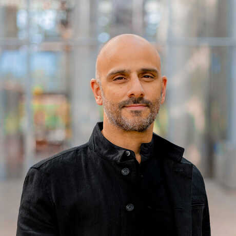 A photo of Sina Mossayeb standing wearing a black coat inside the Academy's Piazza