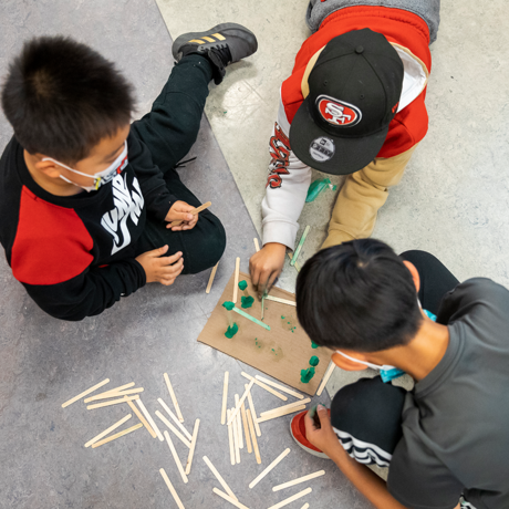 Three children building together with popsicle sticks