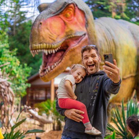 Cute photo of father taking selfie with toddler with animatronic T. rex in the background at Cal Academy