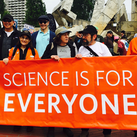 Academy staff stand behind an orange banner that reads "Science is for Everyone"